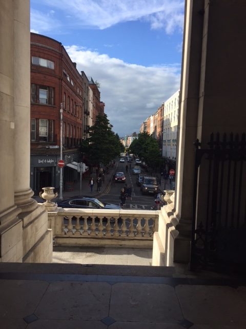 View down urban street from stone building steps
